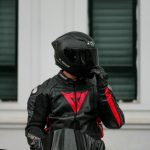 Biker in full black gear riding a sleek motorcycle in an urban setting.