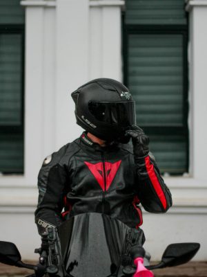 Biker in full black gear riding a sleek motorcycle in an urban setting.