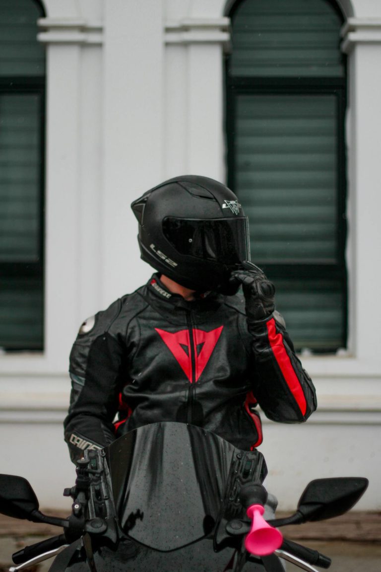 Biker in full black gear riding a sleek motorcycle in an urban setting.